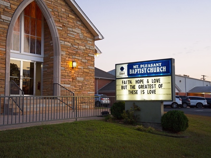 The church at dusk, its lit sign reading “Faith, hope & love, but the greatest of these is love”